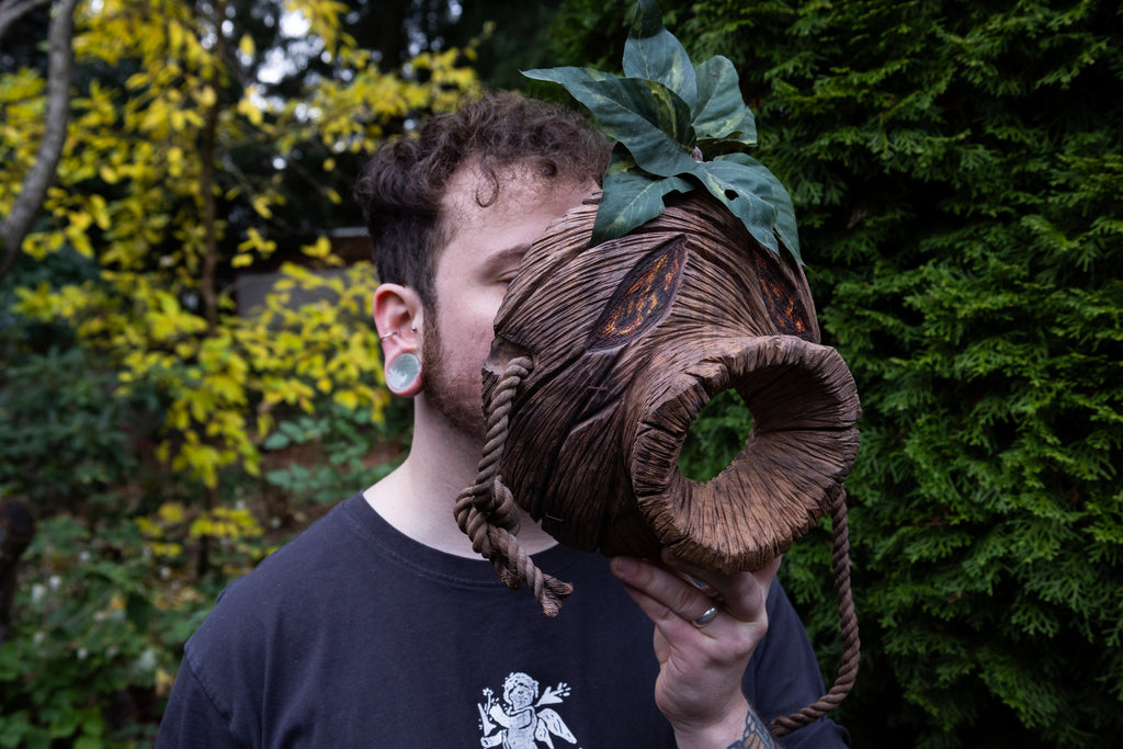 Person with a large wooden head mask holding it to their face