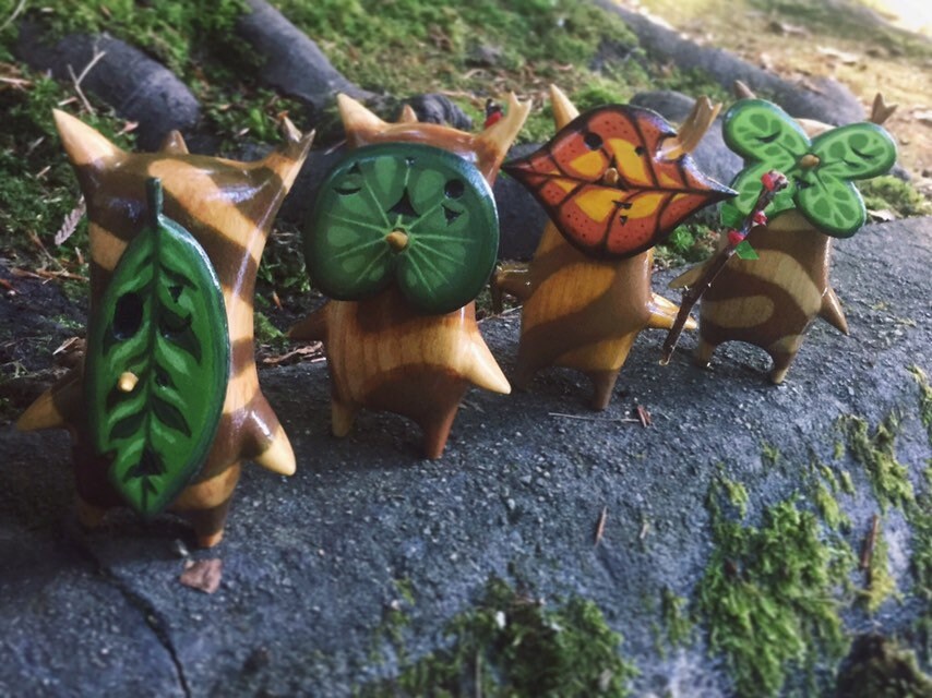 Four small figurines with leaf-like designs on a textured surface