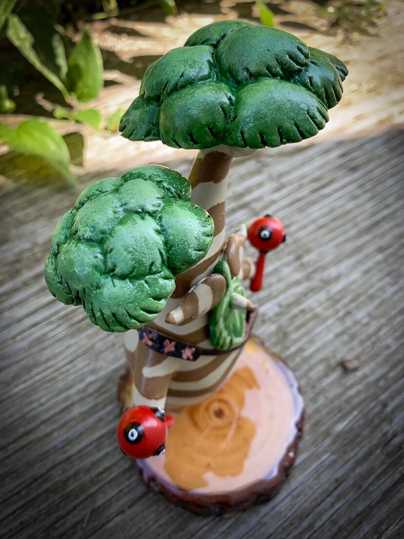 Small figurine with green tree-like structure on a wooden base