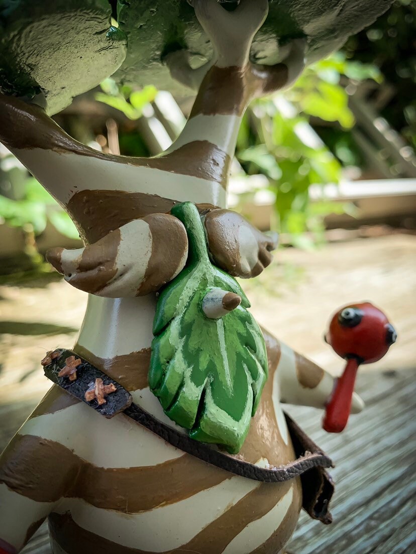 Wooden figurine of a character with a leaf and red object, outdoors.