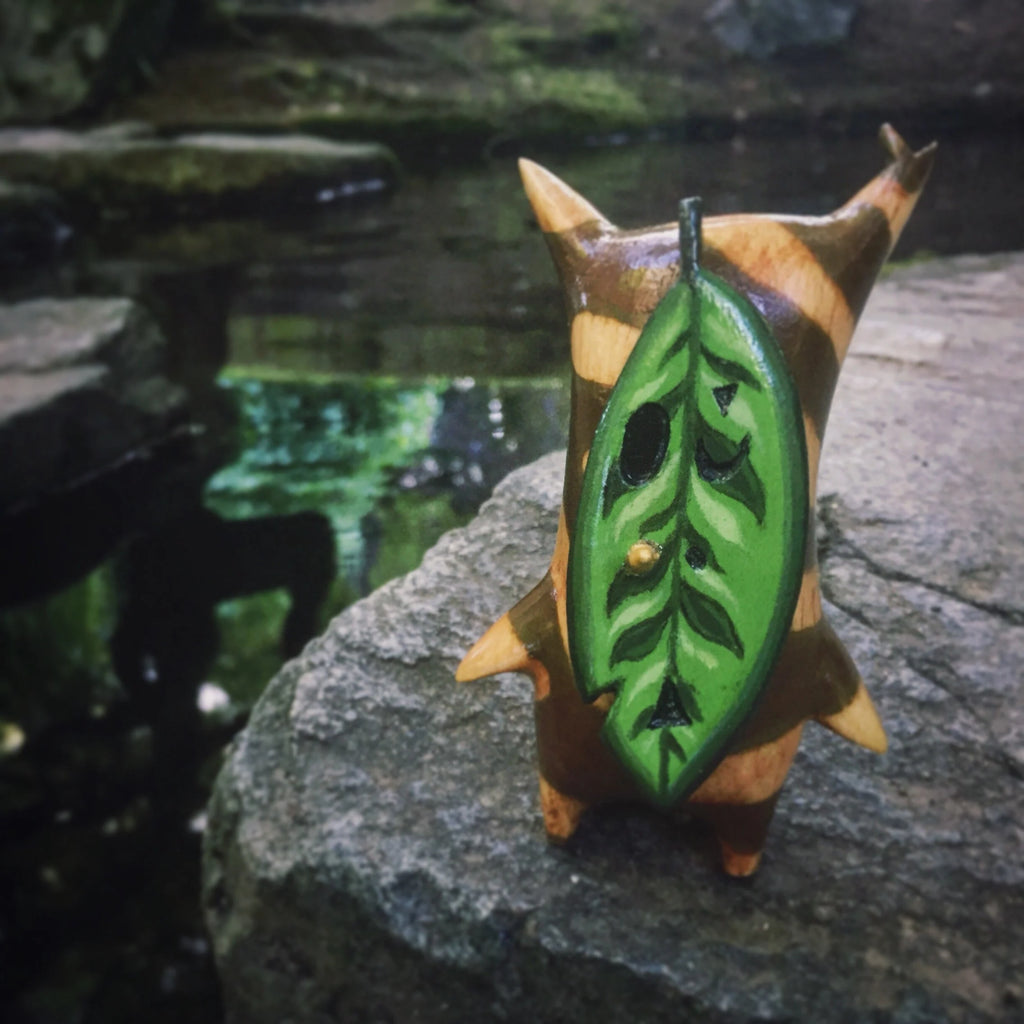 Small wooden korok figurine with a green leaf design on a stone surface
