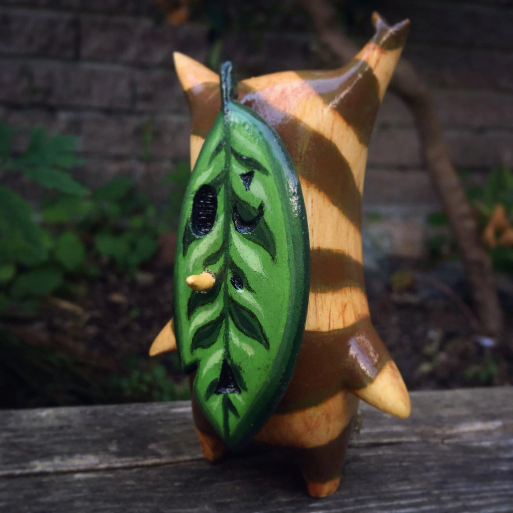 Wooden Korok figurine with a green leaf-like attachment on a wooden surface