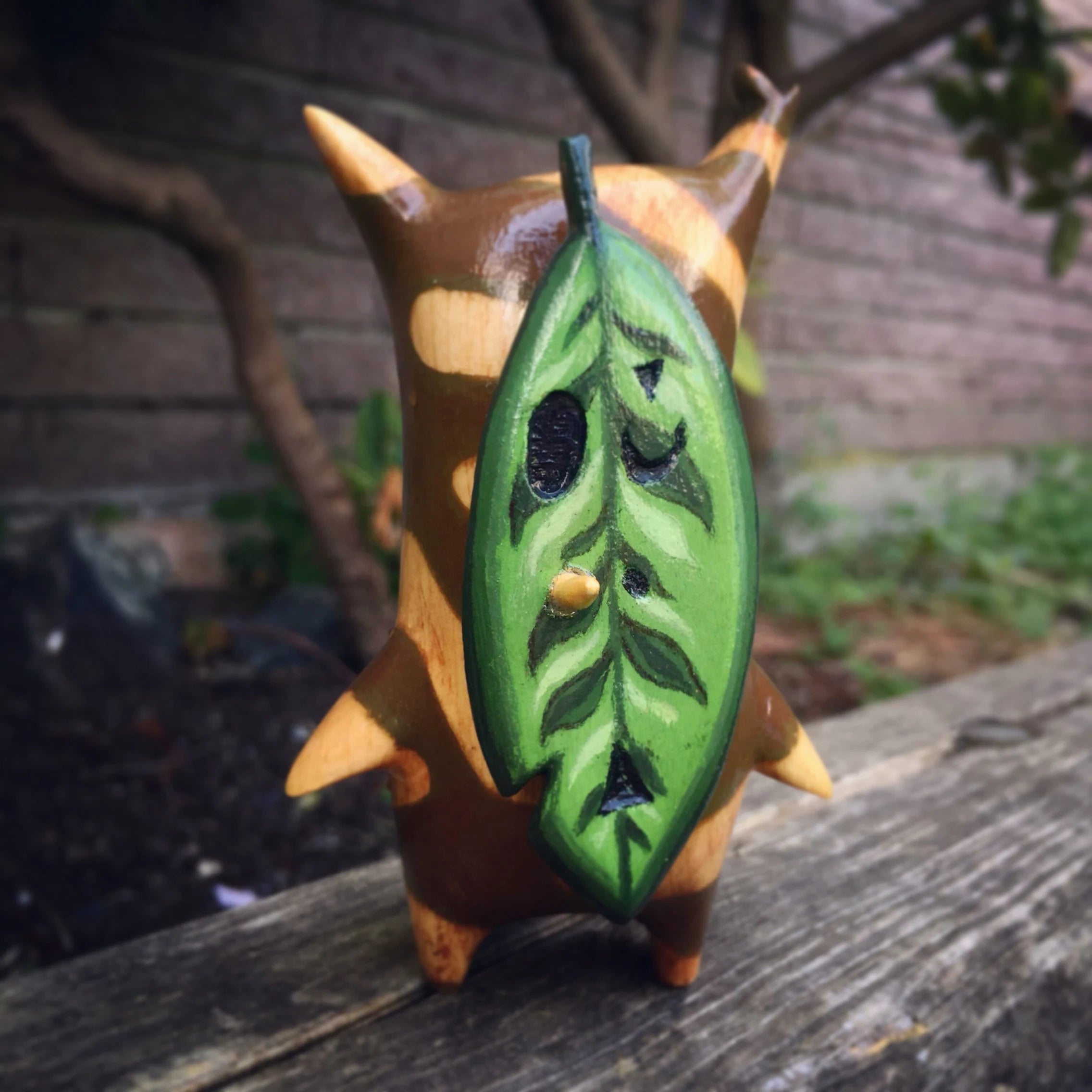 Small Korok figurine with a green leaf-like design on a wooden surface