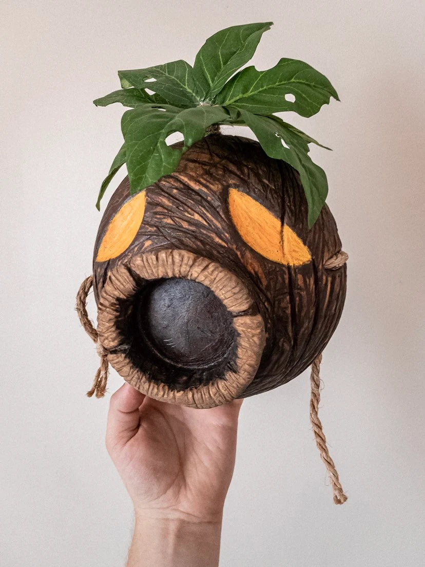 Hand holding a Deku Mask with leaves on a plain background