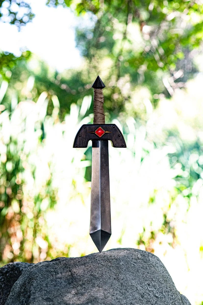 Decorative Kokiri sword with a red emblem on a rock against a blurred green forest background