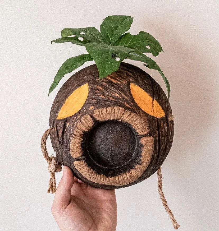 Hand holding a decorative Deku mask with leaves and yellow accents against a light background