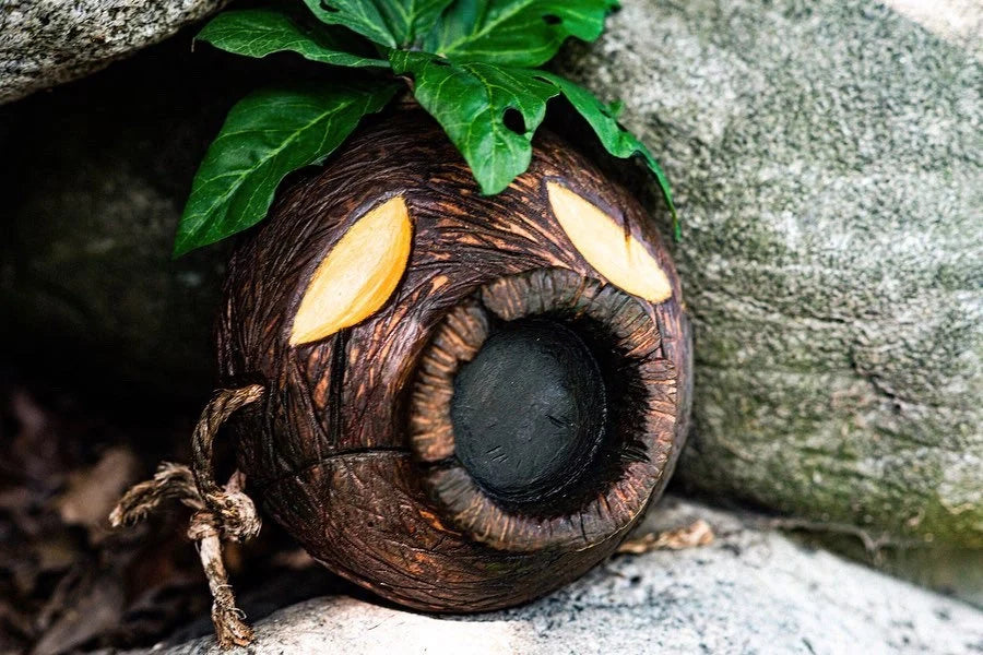 Wooden Deku Mask with glowing like eyes, placed among rocks.