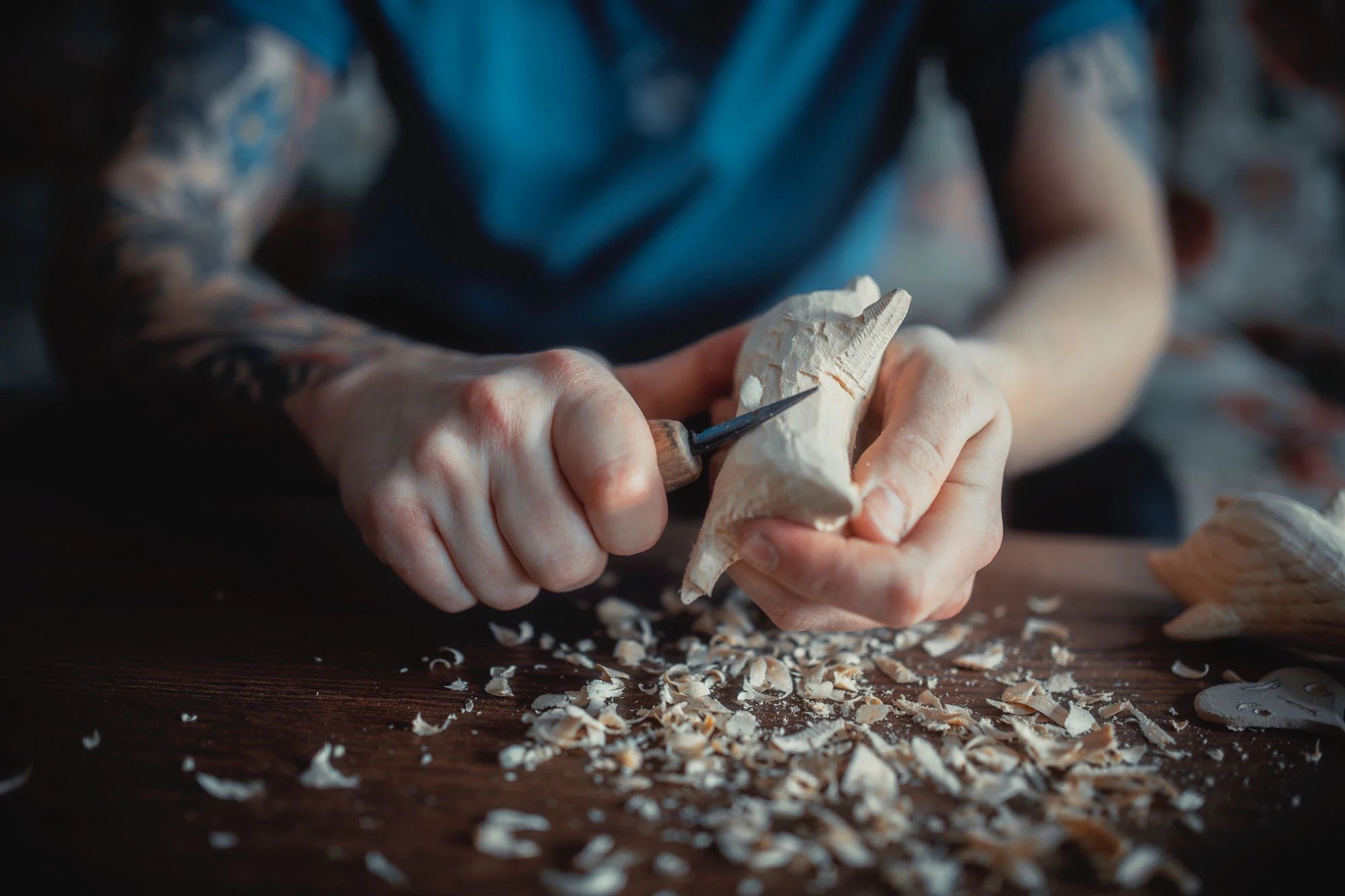 Person carving a wooden figurine with a chisel on a wooden surface