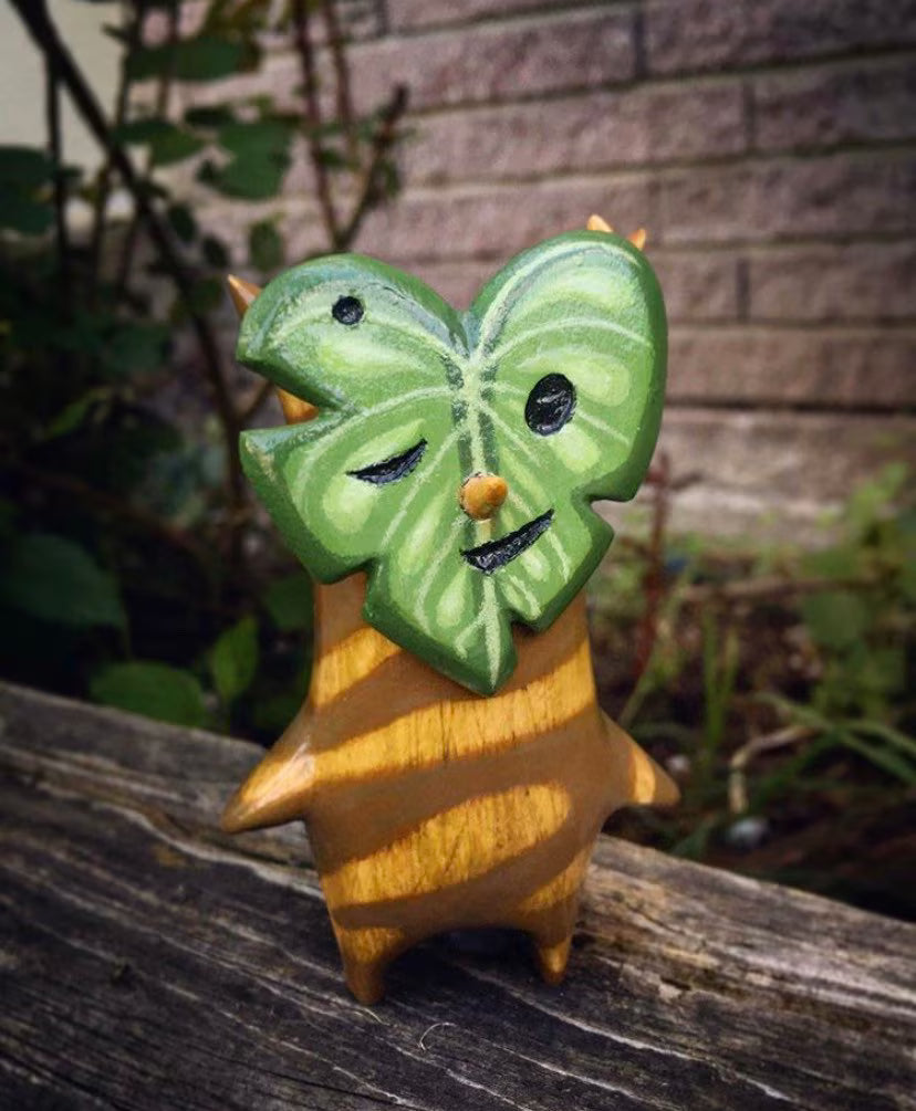 Wooden Korok figure with leaf mask in front of wooden surface.