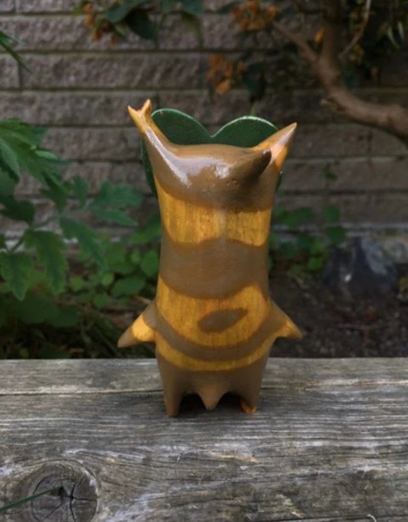 Back of korok statue with a stone wall and plants in the background