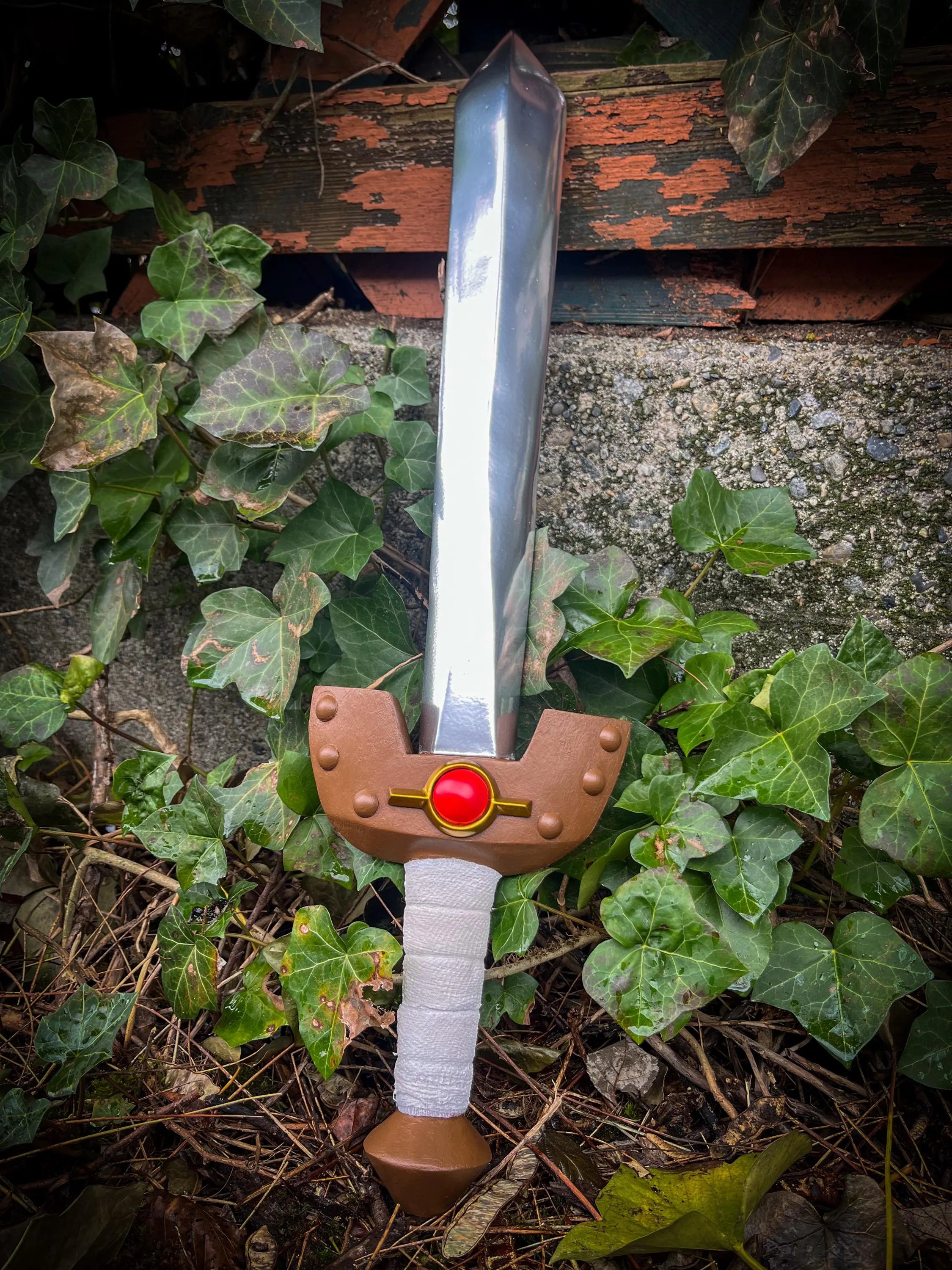 Wooden Kokiri sword with a brown handle and red gem on a stone surface with green leaves.