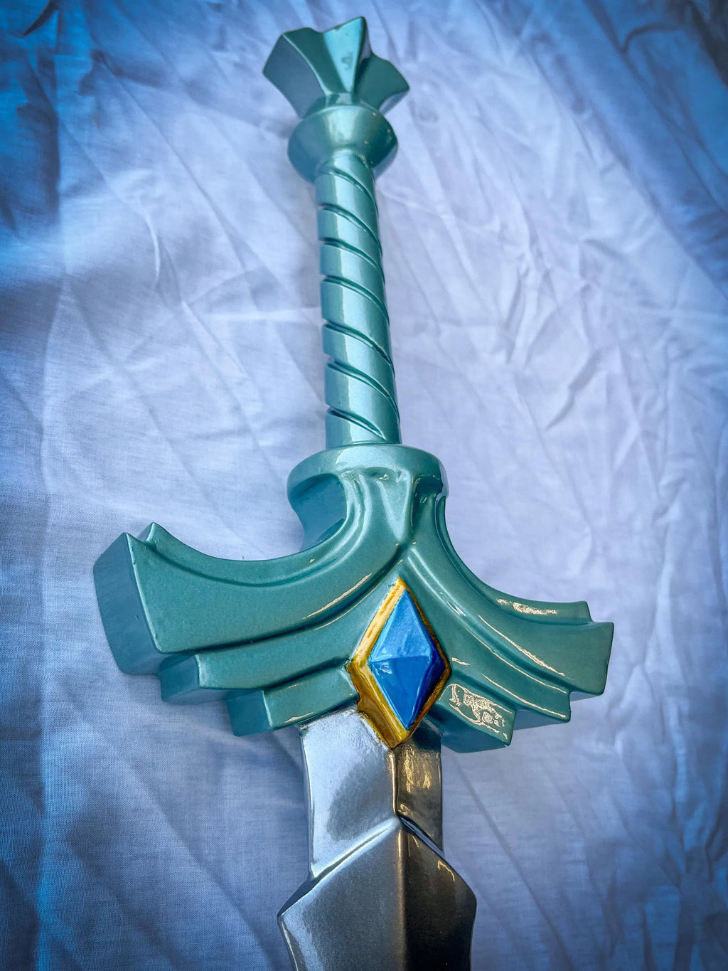 Teal toy sword with a blue gem on a textured white background