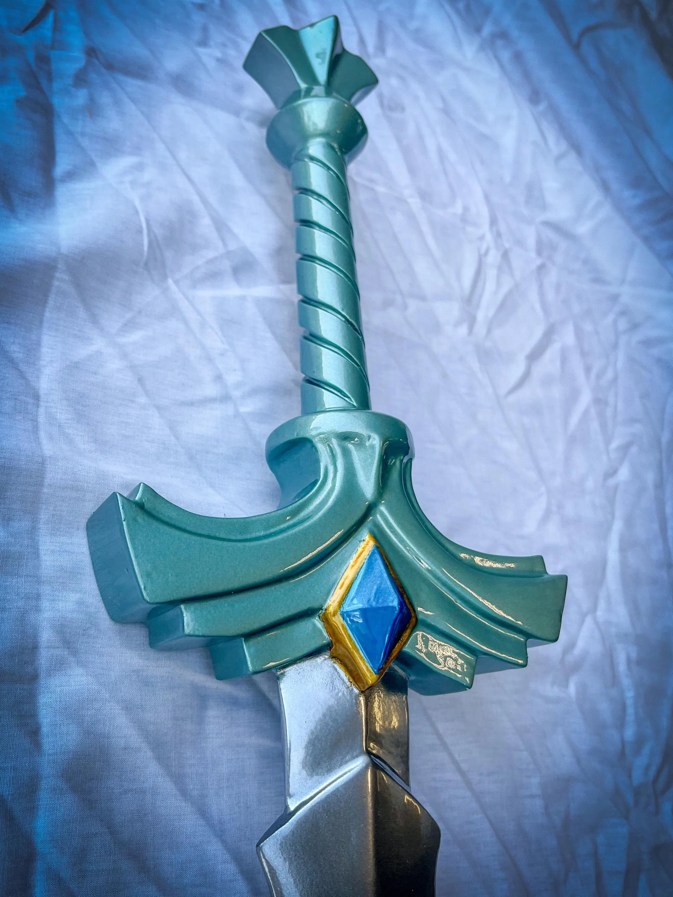 Teal toy sword with a blue gem on a textured white background